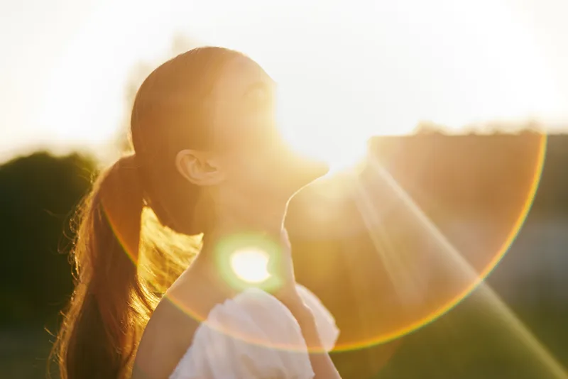 Beautiful young woman basking in golden sunlight with a serene expression, portraying the essence of summer happiness and natural beauty