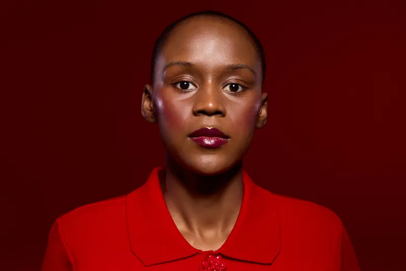 Portrait of confident dark skinned African woman wearing red shirt on red background. Studio lighting highlights glossy lips and smooth skin. Concept of fashion, beauty, and empowerment.
