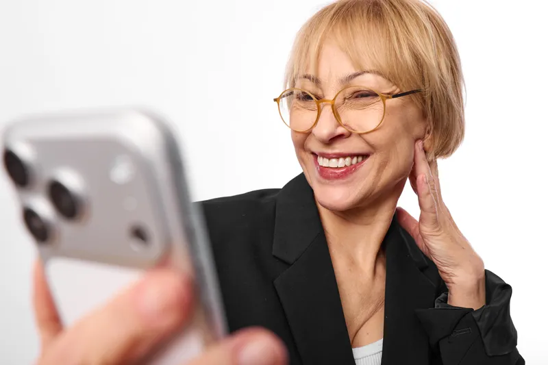 Smiling senior woman with glasses holding a phone, close up portrait on white background, communication concept, friendly business call, soft studio light