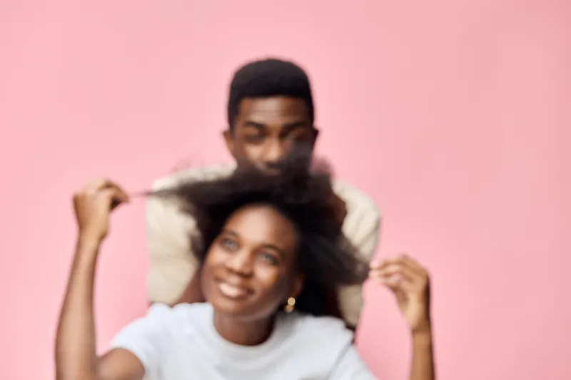 A joyful African couple embracing each other s hairstyles, with a soft pink background, showcasing beautiful natural hair and playful emotions