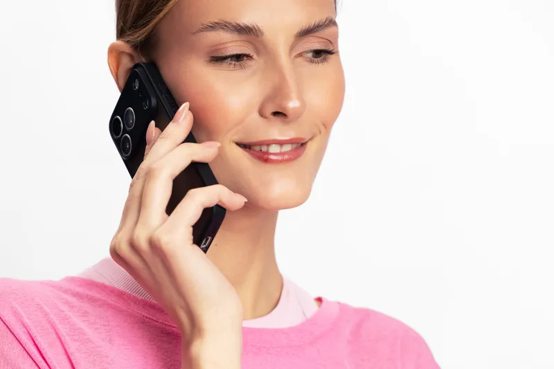 Young woman in pink sweater talking on smartphone with slight smile. Isolated on white background. Concept for communication, technology, mobile phone, and casual conversation.