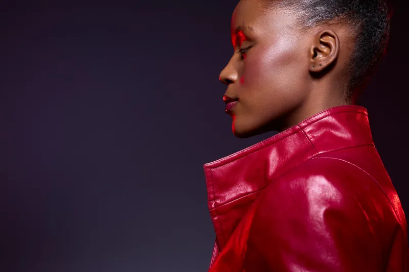Profile of an African woman with dark skin wearing a shiny red leather jacket against a dark purple background. Concept of fashion, beauty, confidence, and stylish urban look.