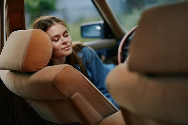 Young woman relaxed in a vintage car, enjoying tranquility and peace, soft colors and natural light enhancing her serene expression and cozy atmosphere.