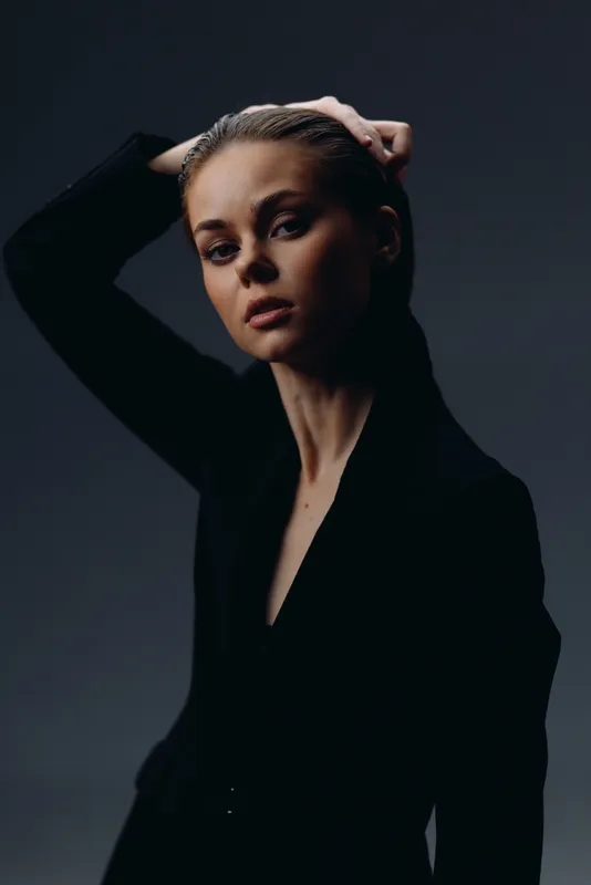 serious woman posing with hand on head in dark stylish clothing against dark background
