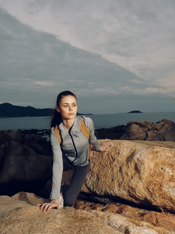 Active woman climbing rocks by the sea, wearing sporty outfit, showcasing determination and focus, set against a serene coastal background