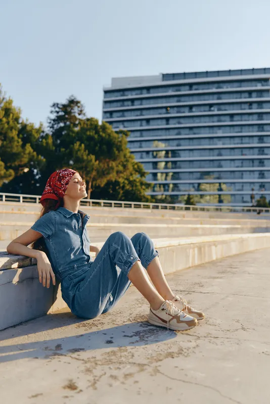 lifestyle woman wearing modern boho-western denim outfit relaxing in urban street style with sunlight and film color effect for casual summer mood