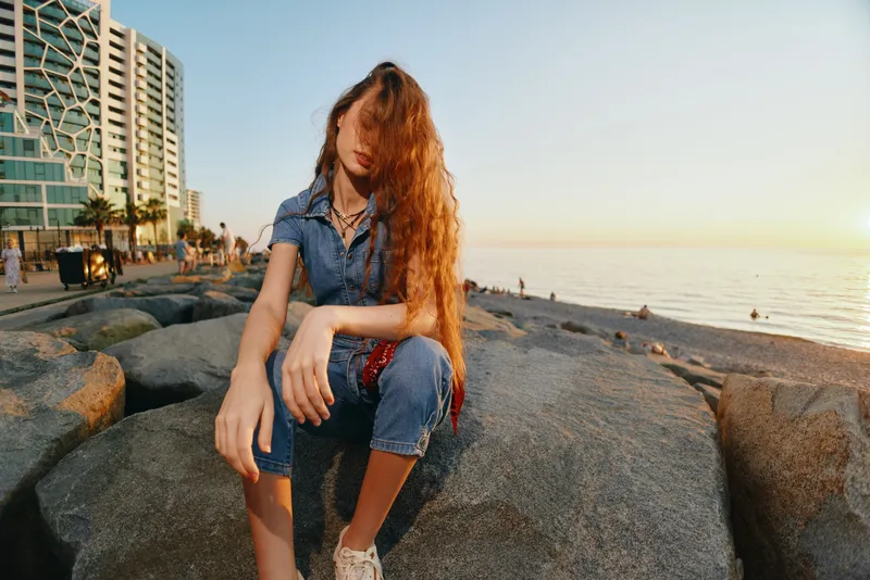 lifestyle woman in modern boho-western denim street style sitting on rocks during golden hour with warm film color tones and relaxed mood