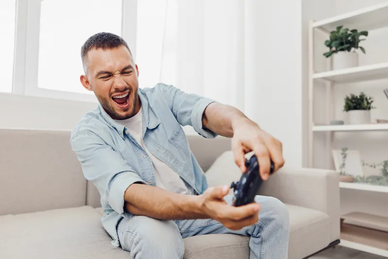 Frustrated man playing video games at home, showcasing emotions of AI anxiety and the challenge of digital detox during leisure time.