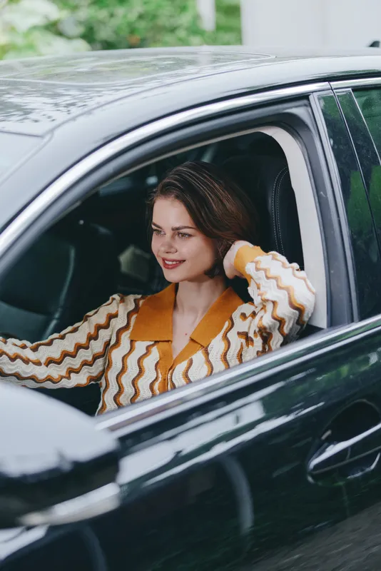 Portrait of a cheerful woman seated in a sleek car, smiling warmly as she rests her hand near the window.