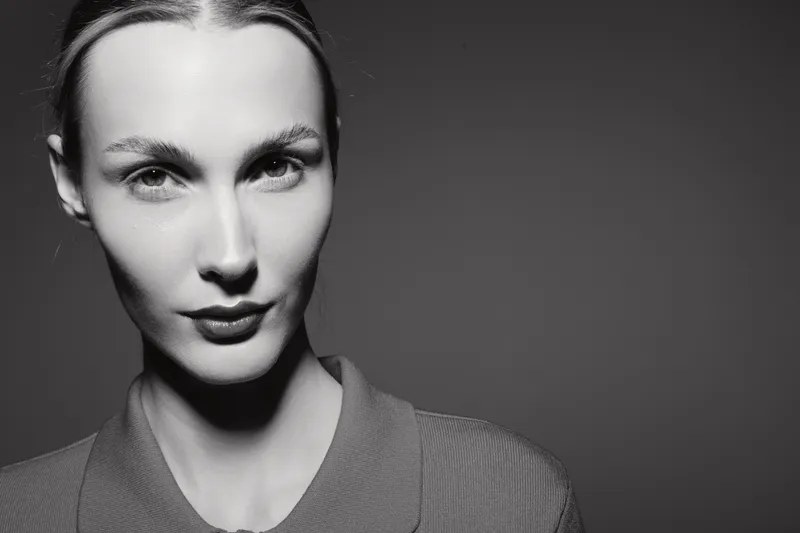 Close-up portrait of a young white woman with light skin and slicked-back hair in black and white studio lighting. Concept of beauty, confidence, and minimalism.