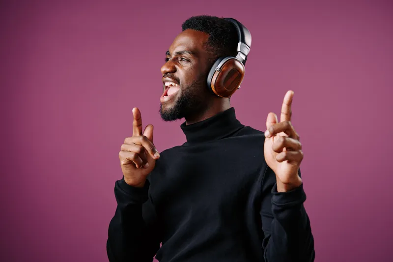 A joyful young African man wearing headphones, enjoying music with a vibrant purple background, radiating energy and happiness while dancing and singing