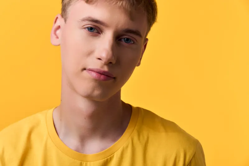 Young man wearing a yellow shirt stands against a vivid yellow background in a soft studio shot, close up face, gentle lighting, and thoughtful expression for lifestyle branding