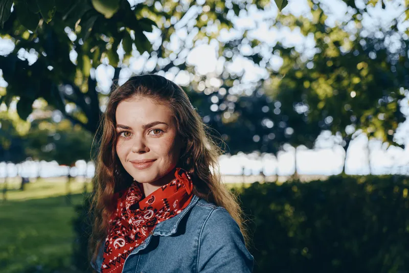 lifestyle woman in modern boho-western denim street style with a red bandana smiling outdoors in natural light with film color effect and greenery background