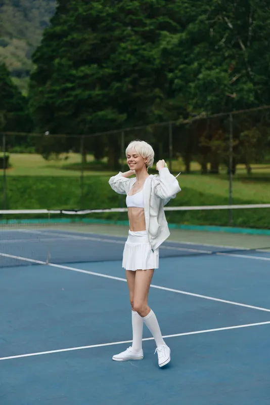Joyful young woman in sporty attire enjoying tennis on a sunny day, showcasing athleticism and confidence with vibrant greens in the background