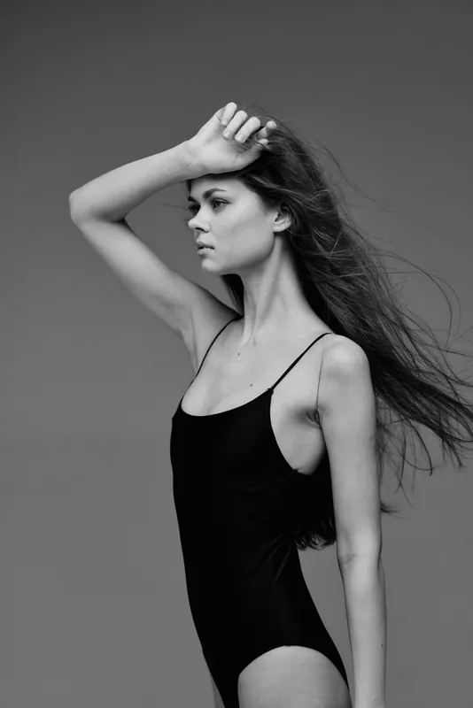 Black and white portrait of a young woman in a black tank top with long flowing hair and a thoughtful expression