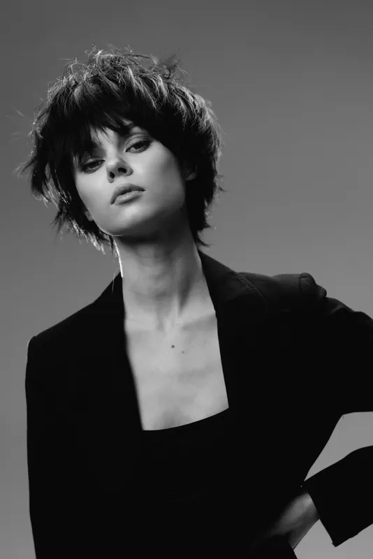 Black and white portrait of a young woman with short hair wearing a blazer, showing confident and stylish expression.