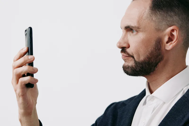 Professional man in business attire stands against an isolated colored background, focused on a smartphone, conveying calm confidence, ambition, and thoughtful communication, suggesting leadership