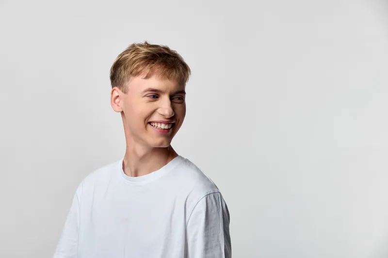 Smiling young man in a white tee in a minimalist studio conveys approachable, friendly mood and casual style, and professionalism for marketing, advertising or stock