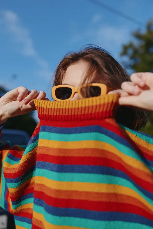 rainbow sweater sunglasses child playful outdoor portrait of a kid pulling a colorful striped sweater over their face while wearing yellow shades under bright blue sky, candid fun moment