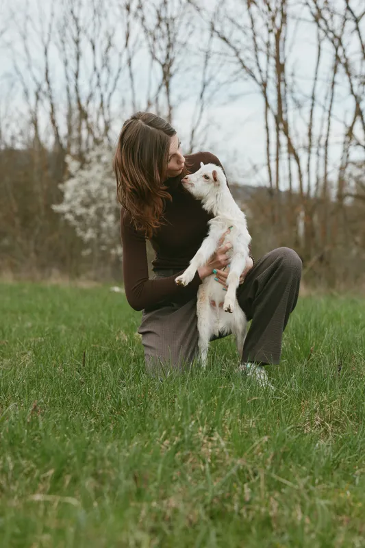 Candid outdoor moment with a woman bonding with a small dog on a grassy field, warm light, soft breeze, casual outfit, natural colors, peaceful nature backdrop