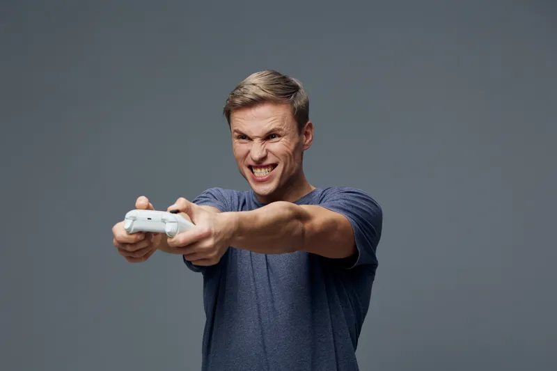 focused young caucasian man playing video games with gamepad wearing blue t-shirt isolated on gray background digital detox entertainment concept