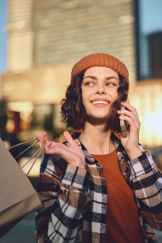 woman shopping on city street, phone to ear and smile, candid moment conveying authenticity and lifestyle during golden hour glow, mindful living and emotional storytelling in urban portrait.