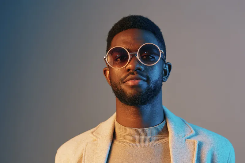 Confident young African man in stylish glasses and modern attire against a gradient background, showcasing contemporary fashion and approachability