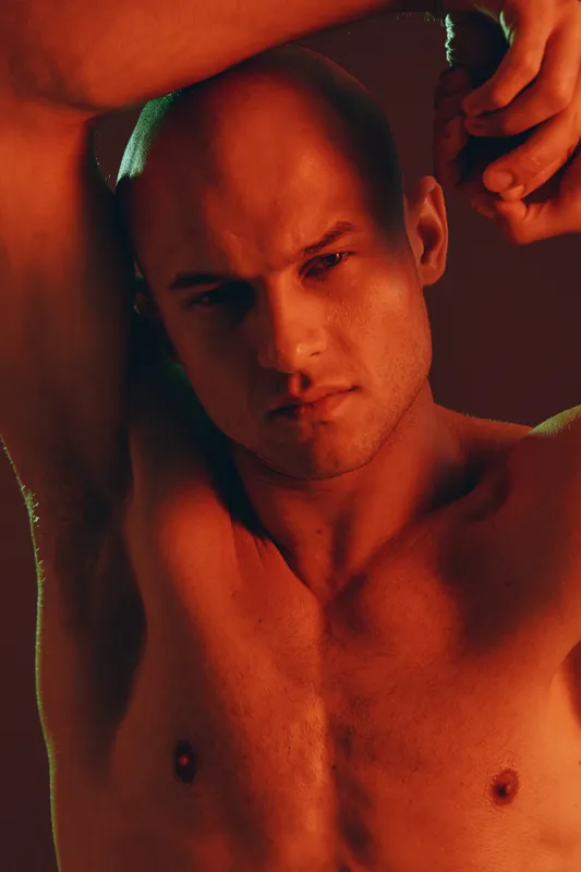 Confident man posing with dramatic lighting, showcasing strong features and a powerful expression. The image explores themes of strength and vulnerability.