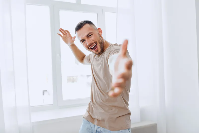 Happy man expressing joy in a bright, airy room, embodying emotional minimalism and soft masculinity while embracing authentic imperfection and self-acceptance.