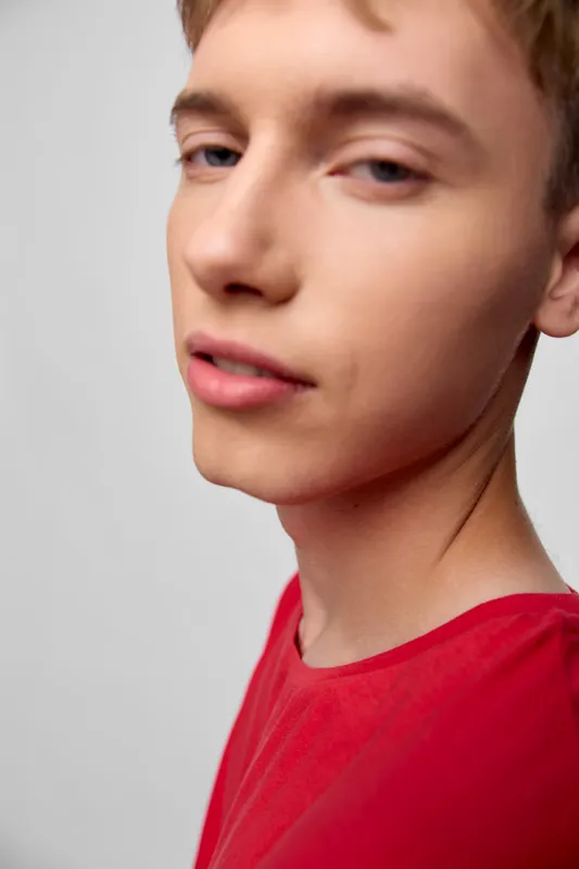 Close up of a young male wearing a red shirt, showcasing a calm facial expression, soft lighting and clean background, ideal for lifestyle, youth fashion and wellness topics