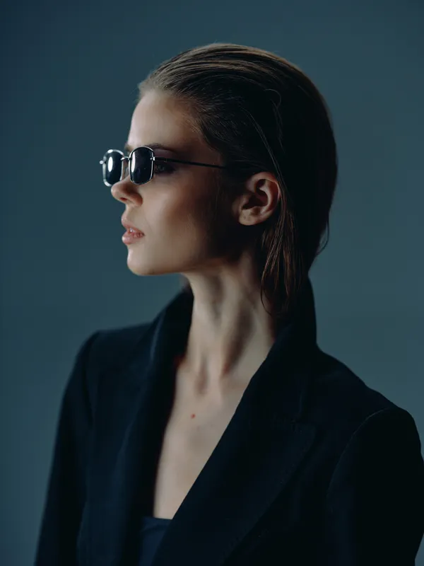 Profile of stylish woman wearing dark sunglasses and black blazer against blue background