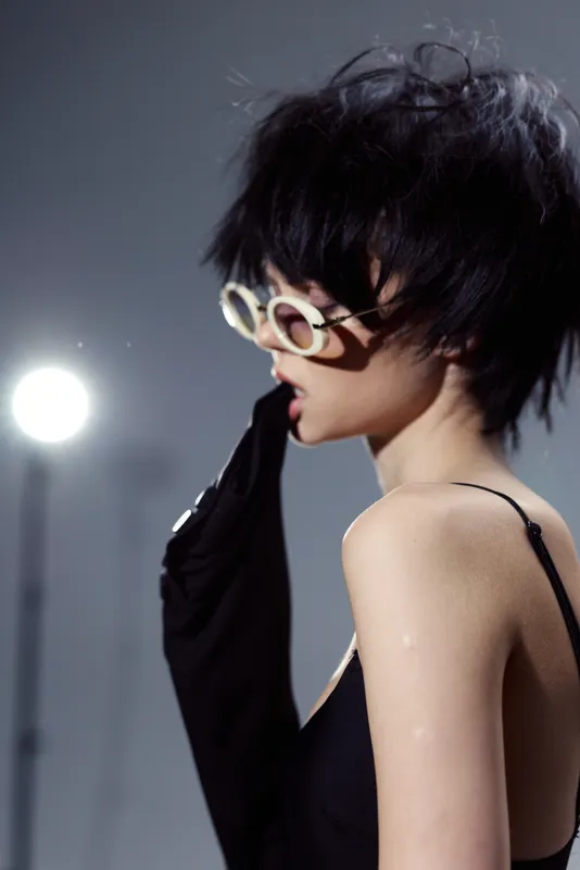 Fashionable woman wearing black dress and round sunglasses in moody studio lighting, stylish, edgy, modern, artistic.