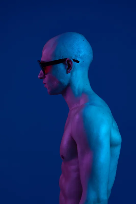 A captivating side profile of a man with sunglasses illuminated by vibrant blue and pink lights, emphasizing his unique features and modern artistic expression.