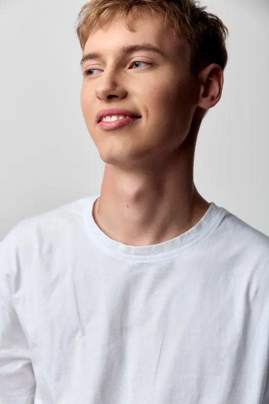 Man with a gentle smile wearing a white t shirt in a bright studio, casual and clean look with relaxed pose, ideal for lifestyle, fashion and wellness themes