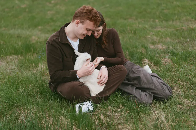 Loving couple sits on grass with a fluffy white dog, sharing a tender moment outdoors, casual outfits, natural light, warm connection, intimate companionship, relaxed lifestyle scene