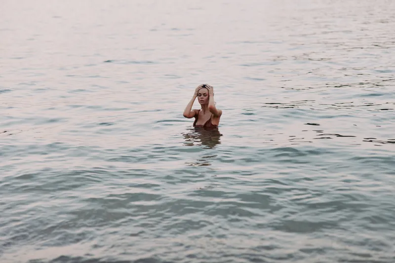 Blonde woman relaxing in calm water at sunset, enjoying peaceful moments and natural beauty with soft light and serene atmosphere.