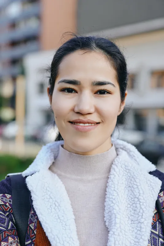 A smiling woman on a city street wearing a warm fleece jacket and light sweater, casual urban style captured in daylight with a busy background and relaxed confidence