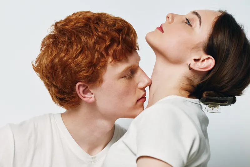 Couple, closeup and intimacy with young man and woman showing affection. Redhead male and brunette female in white clothes on light background for love and connection.