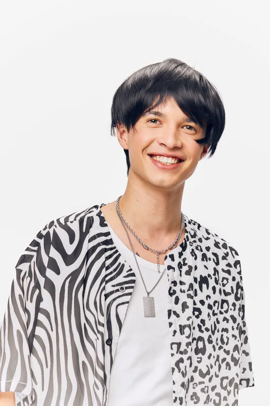smiling man wearing stylish black and white patterned shirt with silver necklaces expressing happiness and youth on a white background in studio lighting