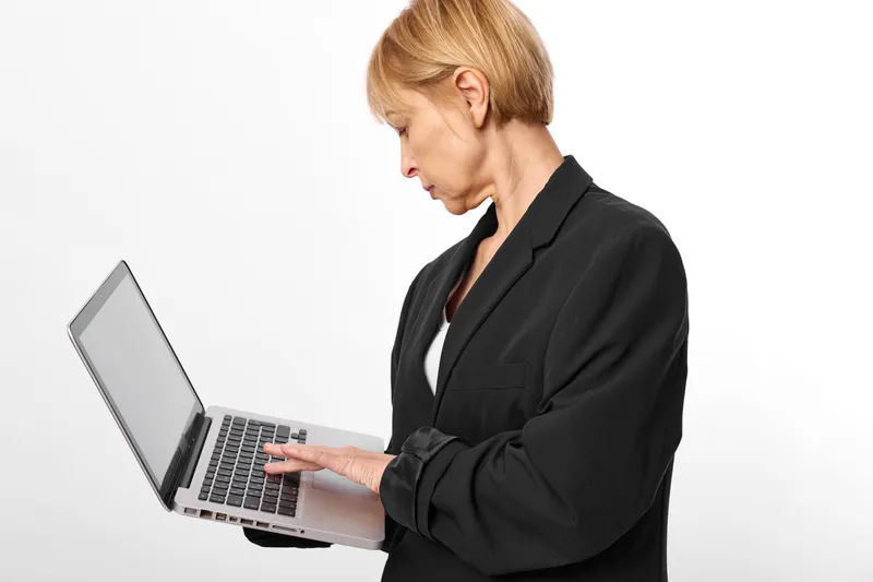 Woman laptop typing in office, corporate business attire, side view. Professional technology worker focuses on computer keyboard for communication, copy space on white background.