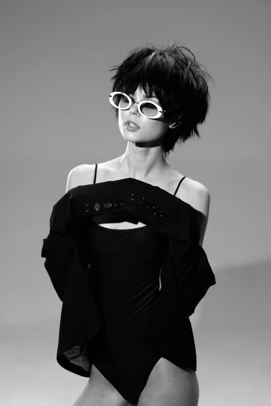 Fashionable woman with short hair wearing white sunglasses and black outfit in black and white style.