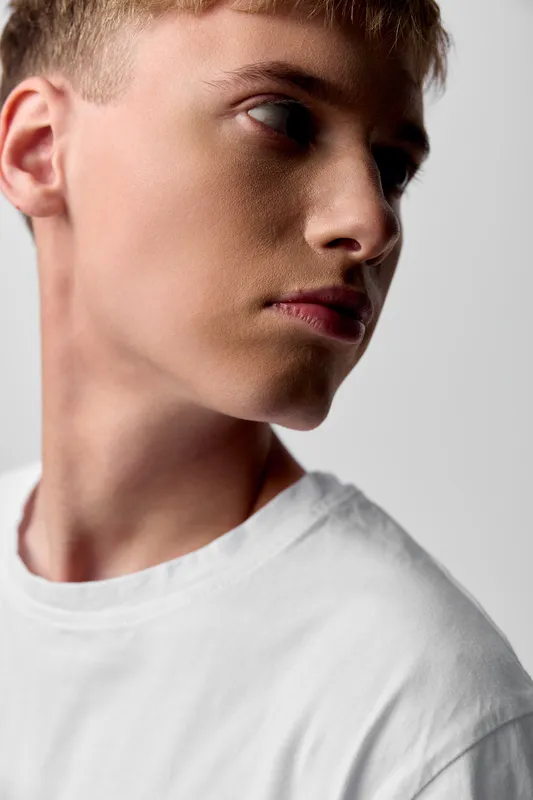 Man in white t-shirt shown in profile with thoughtful expression, close up lighting highlights jawline and skin texture for fashion, editorial, and stock use
