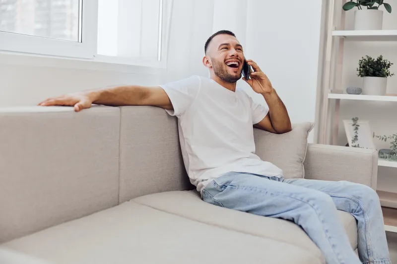 Happy man talking on the phone, expressing emotions while enjoying a relaxing moment at home, reflecting modern life challenges and connections.