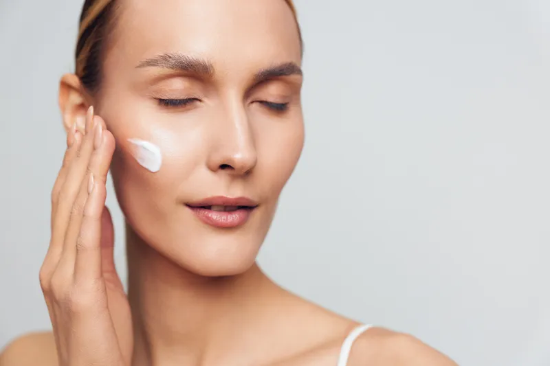 Woman applying white face cream in close up on light background Soft studio lighting highlights skincare wellness self care and clean skin during a gentle facial treatment