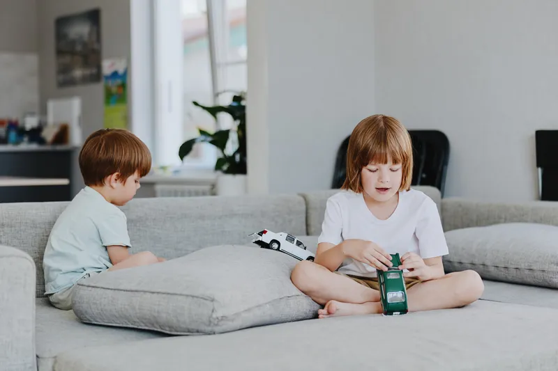 A boy playing with a toy car while sitting on a couch, immersed in a fun activity. The warm, inviting atmosphere highlights childhood joy and creativity.