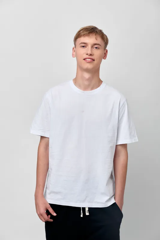 White t shirt worn by a relaxed young man in a studio setting, casual fashion and confident stance, minimal background, ideal for apparel catalogs and lifestyle content.