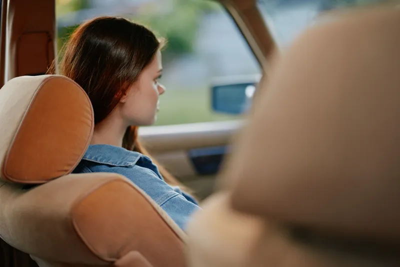 Young woman in casual denim wear relaxing in a car with a thoughtful expression, evoking feelings of contemplation and tranquility in a serene outdoor setting.