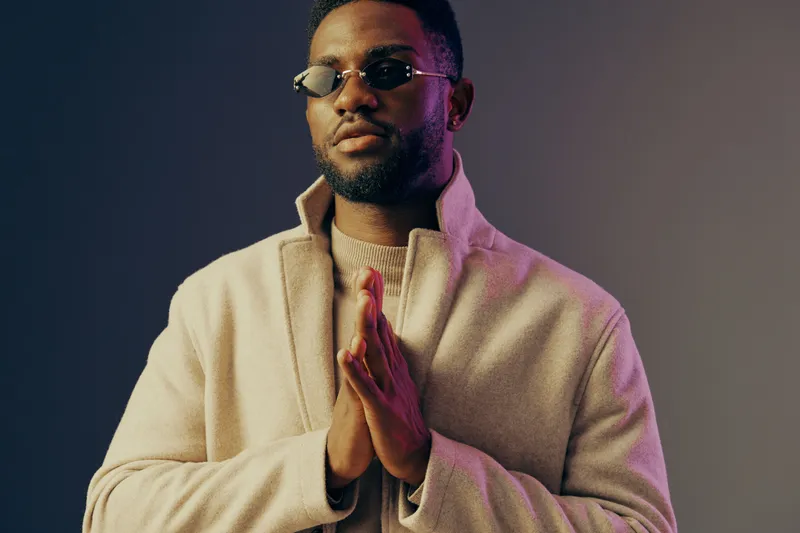 Stylish African American man in sunglasses with hands together against a gradient background, expressing calm and confidence, perfect for lifestyle and fashion themes