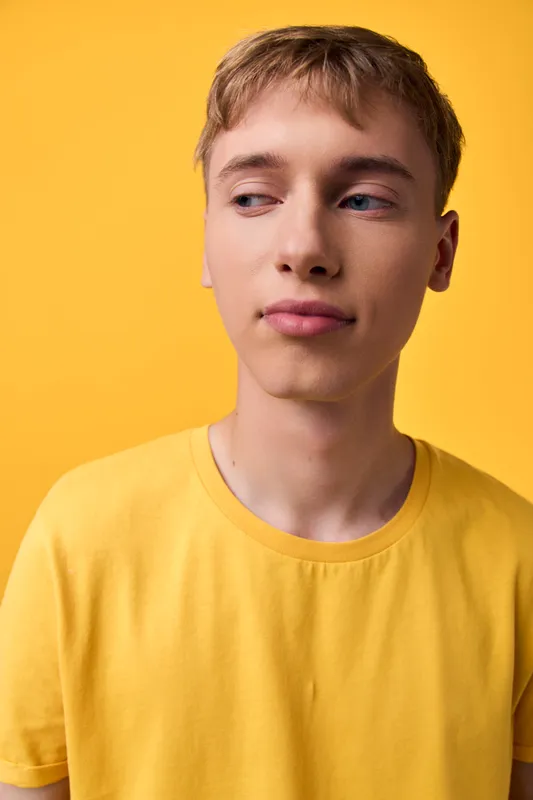 Young man in a yellow shirt against a bright background, showcasing casual style, thoughtful expression, and modern fashion appeal for lifestyle and commercial use in clean studio lighting