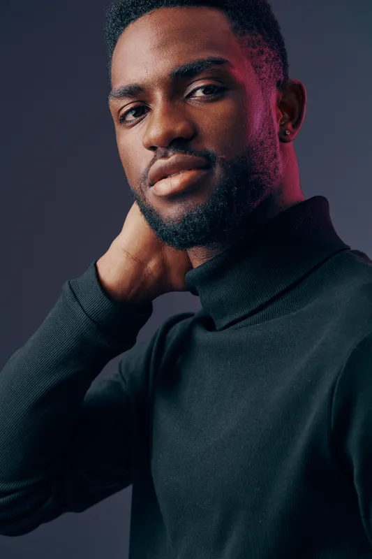 Confident young man in a stylish black turtleneck, showcasing a subtle smile against a dark gradient background, emphasizing modern fashion and self assurance